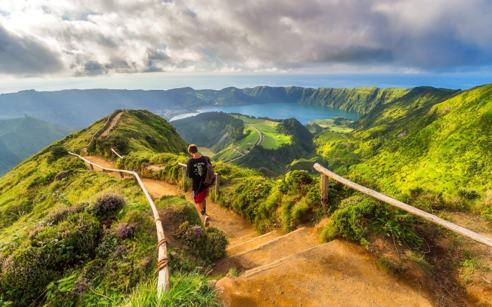A hiker on a ridge trail above the Sete Cidades crater lakes in São Miguel, Azores, with the Atlantic beyond