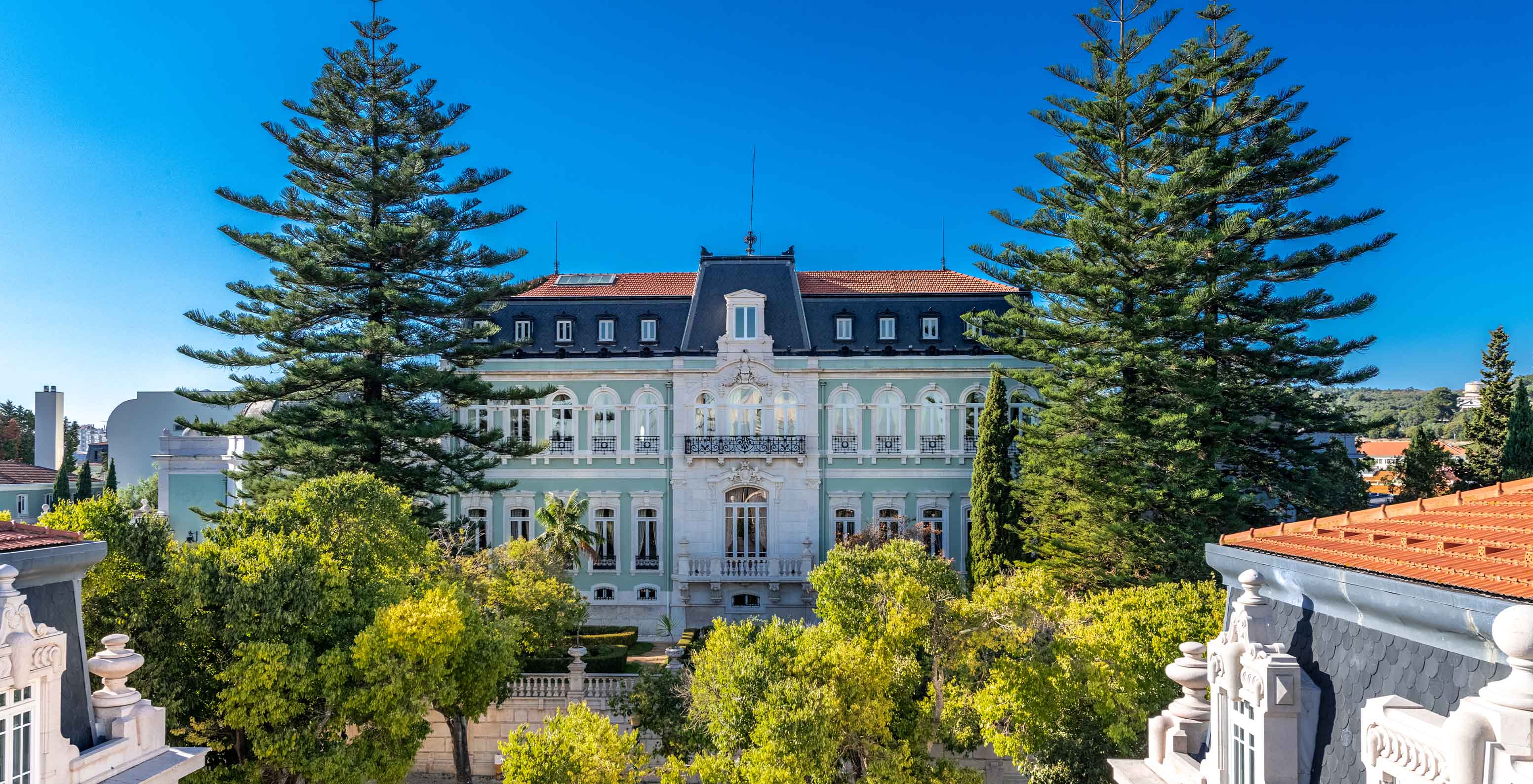 A historic palace hotel facade framed by tall pines near Lisbon